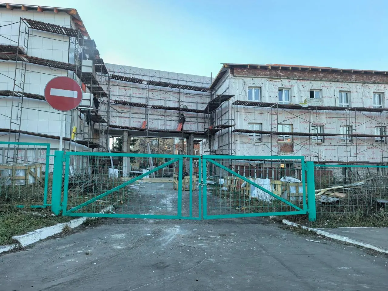 Капитальный ремонт школьного корпуса идёт с задержкой: на кровле продолжаются работы, вокруг — леса и завалы стройматериалов.
